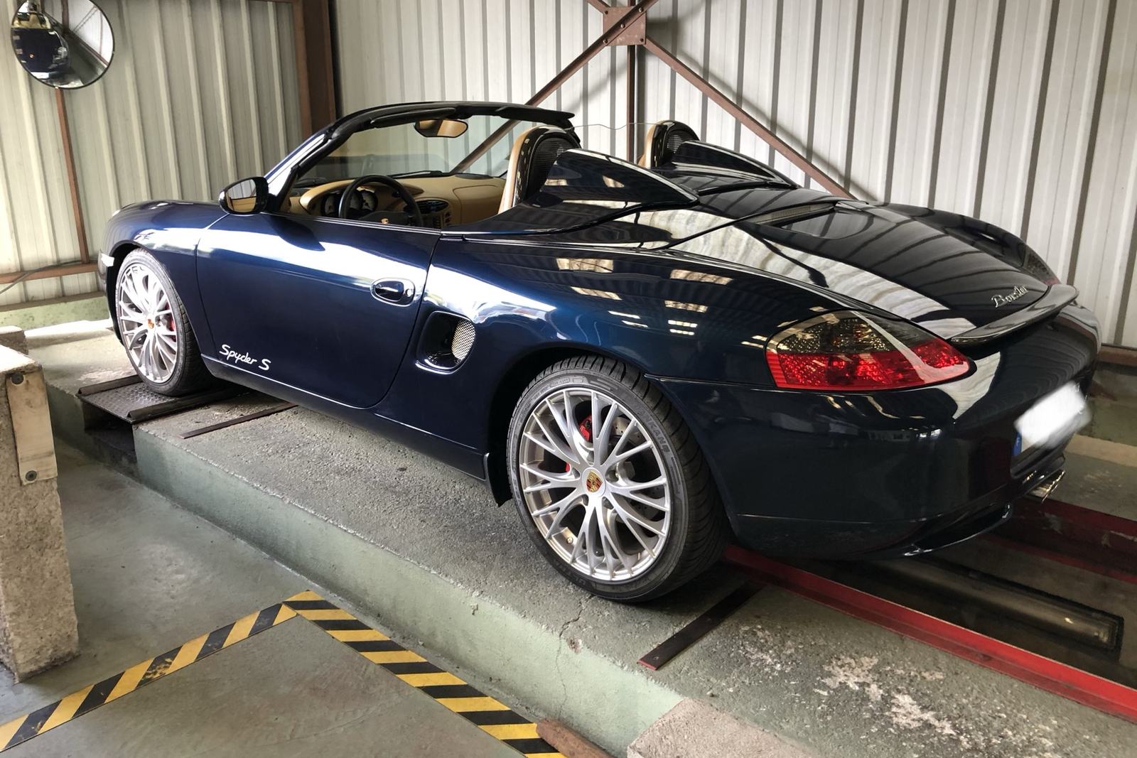 Une Porsche Boxster bleu nuit décapotée, sur le pont de l’atelier